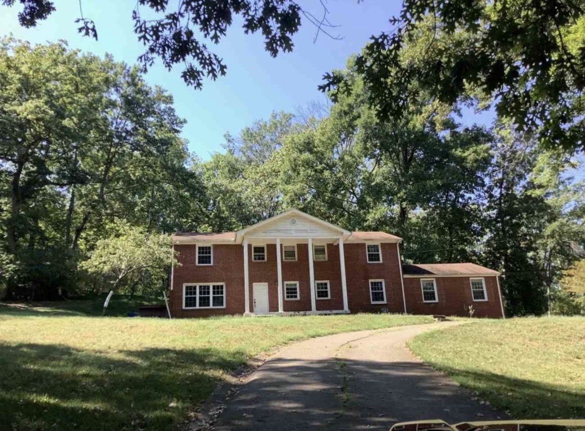 6759 Pennywell Dr, brick colonial with white columns and wooded grounds